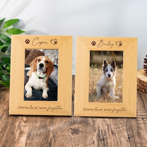 Puede incluir: Dos marcos de fotos de madera clara con fotos de perros. Los marcos tienen grabados los nombres "Cooper" y "Bailey", huellas de patas y un corazón. La frase "Forever loved, never forgotten" está inscrita en la parte inferior.