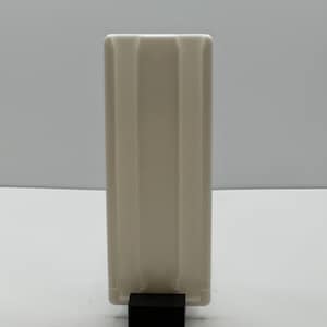 May include: White ceramic rectangular vase with three vertical grooves. The vase is sitting on a black square base.