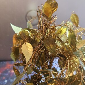 May include: A gold wire tree sculpture with many small gold leaves. The leaves are made of metal and are attached to the wire branches. The sculpture is a decorative piece for a home or office.