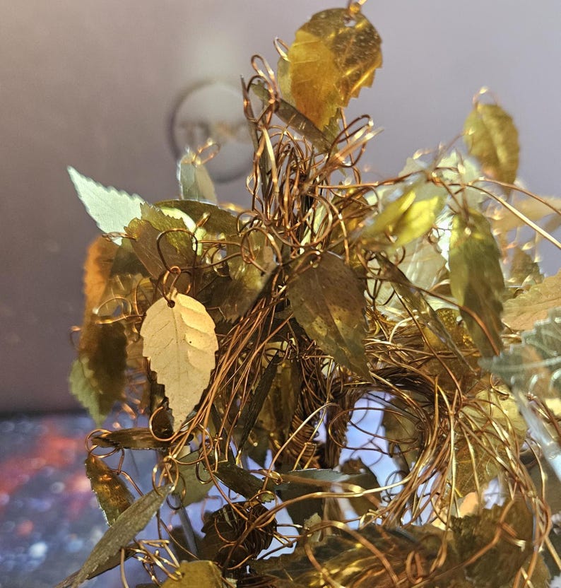 May include: A gold wire tree sculpture with many small gold leaves. The leaves are made of metal and are attached to the wire branches. The sculpture is a decorative piece for a home or office.