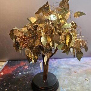 May include: A gold wire tree sculpture with a black base. The tree has many gold leaves and is decorated with gold wire.