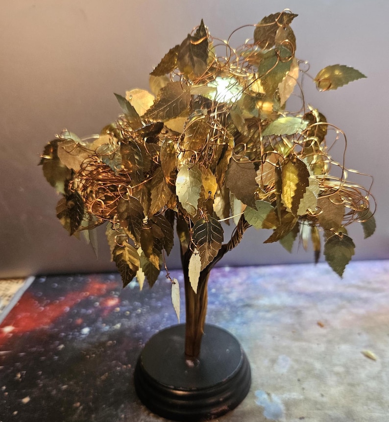 May include: A gold wire tree sculpture with a black base. The tree has many gold leaves and is decorated with gold wire.