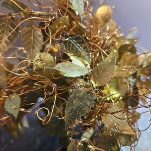 May include: A gold wire sculpture of a tree with many leaves. The leaves are made of metal and are a light gold color. The wire is a darker gold color.