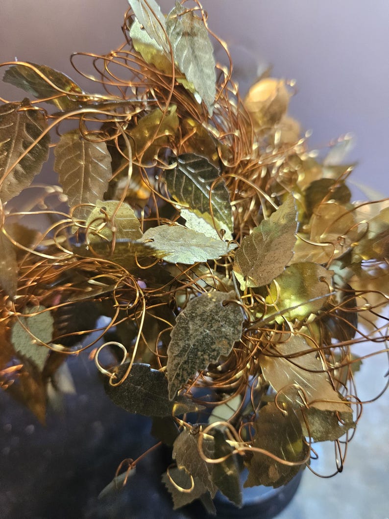May include: A gold wire sculpture of a tree with many leaves. The leaves are made of metal and are a light gold color. The wire is a darker gold color.