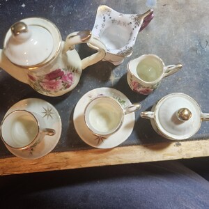 May include: A vintage porcelain tea set with floral designs. The set includes a teapot, creamer, sugar bowl, and two teacups and saucers.
