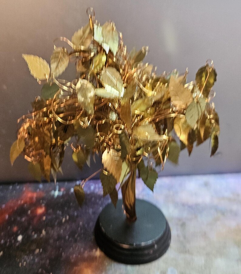 May include: A gold-colored metal tree sculpture with a twisted trunk and many leaves. The tree is on a black circular base.