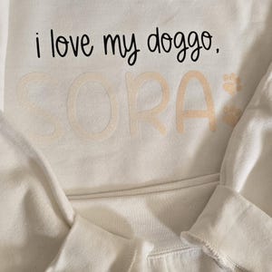May include: White sweatshirt with the text "i love my doggo. SORA" in black and gold glitter lettering.