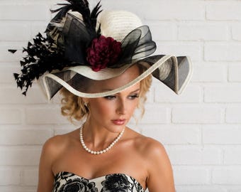 Sombrero de ala ancha, color blanco roto con plumas blancas rotas, lazos de organza negra, flor rojo intenso