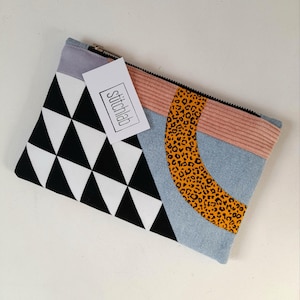 May include: A geometric clutch with a black and white triangle pattern, a light blue denim section, and a peach corduroy stripe. A curved section features a leopard print. The tag reads "stitchlab".