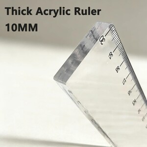 K&ouml;nnte beinhalten: Ein dickes, transparentes Acryl-Lineal mit schwarzen Messmarkierungen und dem Text Thick Acrylic Ruler 10MM an der Seite. Das Lineal weist eine sichtbare Dicke von 10 mm sowie klare numerische Abstufungen entlang der Kante f&uuml;r pr&auml;zise Messungen auf.