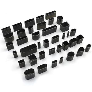 May include: A collection of various black metal craft punches in different shapes and sizes, including rectangles, squares, circles, and ovals. The punches are arranged on a white surface.