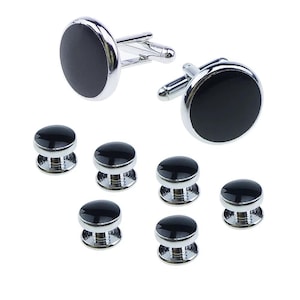 May include: A set of black and silver cufflinks and shirt studs. The cufflinks have a circular black face with a silver border and a silver clasp. The shirt studs have a similar design, with a black circular face and a silver base.