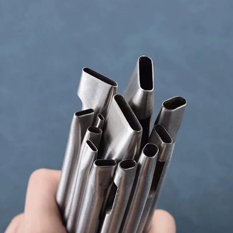 May include: A collection of stainless steel oval-shaped leather punches, varying in size. The tools are held together, with the open ends of the punches facing the viewer. The background is a solid, muted blue.