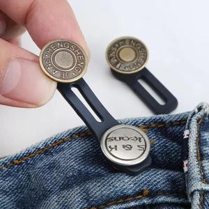 May include: Two sets of jean button extenders. One extender is attached to denim. The extenders have a black elastic loop and a metal button with the text "HENG SHENG" and "S & K JEANS".