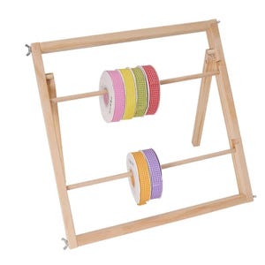 May include: A light-colored wooden ribbon organizer stand featuring two horizontal dowels. The top dowel holds four spools of gingham ribbon in pink, yellow, green, and red. The bottom dowel holds two spools of gingham ribbon in orange and purple.