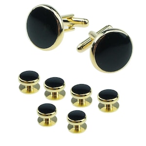May include: A set of gold-toned cufflinks and shirt studs. The cufflinks and studs have a black, circular center with a gold-colored border. The shirt studs have a smaller profile than the cufflinks.