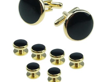 May include: A set of gold-toned cufflinks and shirt studs. The cufflinks and studs have a black, circular center with a gold-colored border. The shirt studs have a smaller profile than the cufflinks.