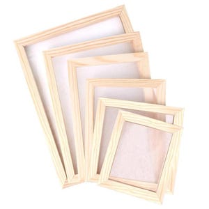 May include: A collection of five wooden artist canvas frames of varying sizes, arranged in a diagonal pattern. The frames are made of light-colored wood and have a white canvas stretched across them. The frames are empty and ready for painting.