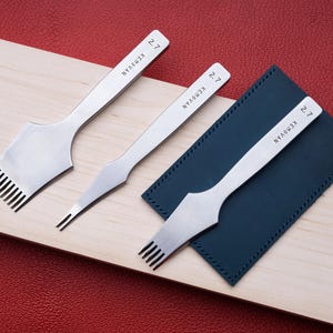 May include: Three silver-colored metal leather stitching chisels with the brand name KEMOVAN and the number 2.7 engraved on the handles. The set includes one wide multi-prong chisel, one narrow two-prong chisel, and one medium multi-prong chisel.