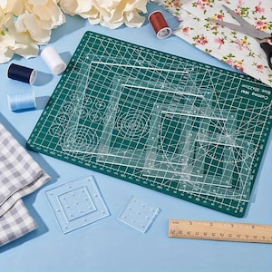 May include: A set of clear acrylic quilting templates in various square sizes arranged on a green cutting mat with grid lines. The set includes two small square templates with pin holes, a wooden ruler measuring 20 cm, and sewing supplies.