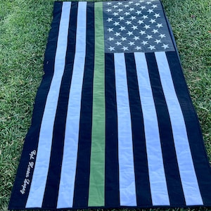 May include: Black and white American flag with a green stripe down the center. The flag is made of fabric and has a white embroidered text that reads "Old Glory Forever".