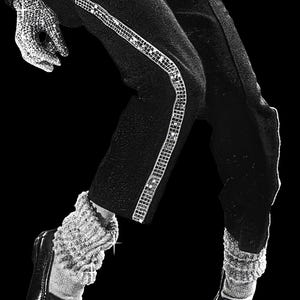 May include: Black and white image of a person in a performance outfit. The outfit includes black pants with a sequined stripe, a sequined glove, and black shoes. The socks are white and textured.
