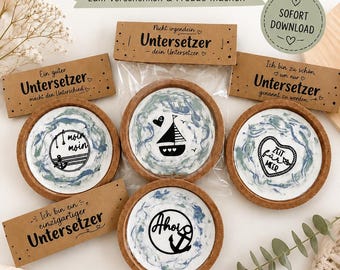 May include: Four round coasters with cork edges and white centers featuring blue and green marbled patterns. Each coaster displays a black graphic: a sailboat, an anchor with the text Ahoi, a heart with the text Zeit für Meer, and a buoy with the text Moin Moin. The set includes four brown paper labels with German text.