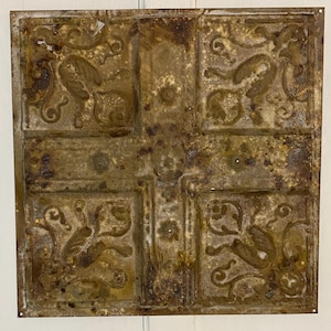 May include: A square, antique metal ceiling tile with a distressed, aged appearance. The tile is divided into nine squares, each featuring embossed floral and scrollwork designs. The metal has a mottled, brown and gold patina, with signs of rust.
