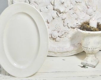 May include: A large, white oval serving platter with a slightly raised rim. The platter is made of ceramic and has a smooth, glossy finish.