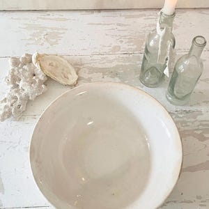 Peut inclure: Un grand bol en c&eacute;ramique blanc cass&eacute; avec un aspect l&eacute;g&egrave;rement vieilli. &Agrave; c&ocirc;t&eacute;, deux bouteilles en verre transparent, dont une avec une bougie allum&eacute;e. Un morceau de corail et une coquille d'hu&icirc;tre compl&egrave;tent le th&egrave;me rustique et c&ocirc;tier.