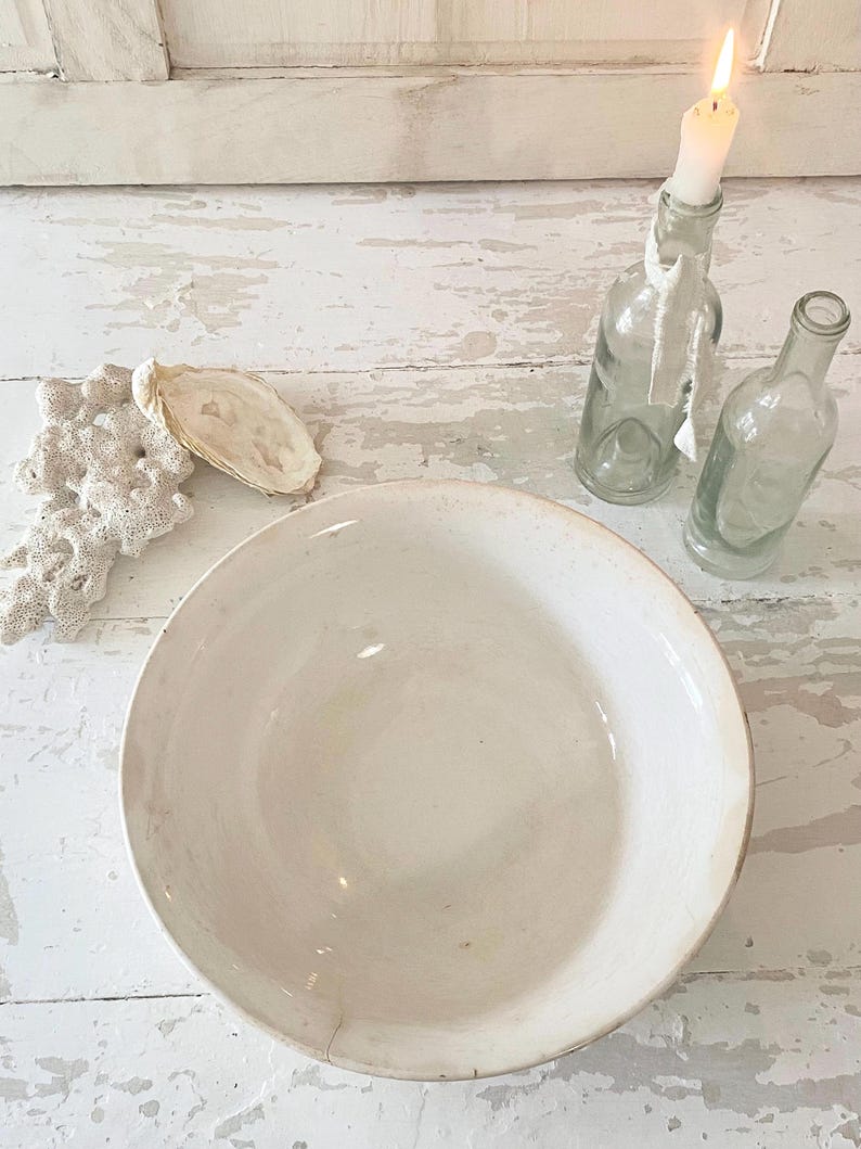 Peut inclure: Un grand bol en c&eacute;ramique blanc cass&eacute; avec un aspect l&eacute;g&egrave;rement vieilli. &Agrave; c&ocirc;t&eacute;, deux bouteilles en verre transparent, dont une avec une bougie allum&eacute;e. Un morceau de corail et une coquille d'hu&icirc;tre compl&egrave;tent le th&egrave;me rustique et c&ocirc;tier.