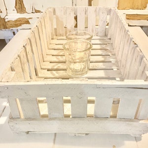 May include: White wooden crate with two clear glass candle holders. The crate has a rustic, distressed look and is ideal for displaying small items.