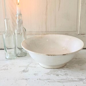 Peut inclure: Un grand bol en c&eacute;ramique blanche avec un large bord repose sur une surface en bois blanc vieilli. Deux bouteilles en verre transparent et une bougie allum&eacute;e dans une bouteille en verre sont derri&egrave;re le bol. La bougie a une flamme vive.