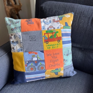May include: Square patchwork pillow with various fabric squares. The pillow features colorful squares with images of trucks, planes, and text that reads "SOME DUDE", "GRANDMA'S OR BUST!", "We Love You Elijah & Charlie", and "WROOM!".