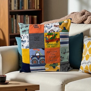 May include: A patchwork pillow with various fabric squares featuring vehicle designs and the text "SOME DUDE", "GRANDMA'S OR BUST!", and "We Love You Elijah Charlie". The pillow is on a white couch with other decorative pillows.