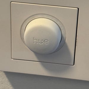 May include: A white light switch with a round, white button that says "hue" on it.