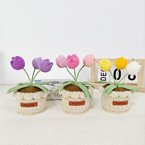 May include: Three crocheted flower arrangements in pots. The flowers are pink, purple, and yellow. Each pot has a brown label that says "Handmade".