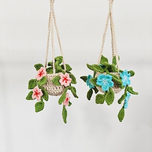 May include: Two hanging crochet plant holders. One features pink flowers and the other has blue flowers. Both have green leaves and are suspended by beige macrame cords. The crochet baskets are a light beige color.