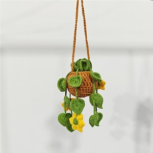 Pode incluir: Um vaso de plantas pendurado de crochê com folhas verdes e flores amarelas. O vaso é marrom e tem um suporte de corda.