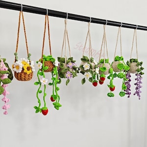 May include: A collection of handmade crochet hanging baskets, each filled with colorful flowers and trailing vines. The baskets are in various shades of brown, green, and white, with accents of yellow, red, and purple. The baskets are suspended from a black rod.