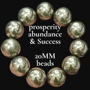 May include: A circular arrangement of eleven large, reflective, metallic-toned spherical beads. The center of the image features the white text "prosperity abundance & Success" followed by "20MM beads" below it, all set against a solid black background.