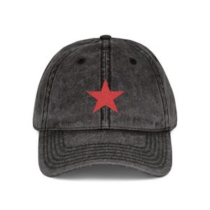 Può includere: Un cappellino da baseball grigio antracite con una stella rossa ricamata sul davanti. Il cappellino ha una visiera curva e un aspetto vintage e usurato. La stella è centrata sul pannello frontale.