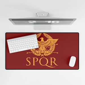 Puede incluir: Alfombrilla de escritorio rectangular con fondo burdeos y un emblema dorado con un águila y las letras SPQR. Un teclado y un ratón blancos están sobre la alfombrilla. Un monitor de ordenador está encima de la alfombrilla.