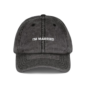 Könnte beinhalten: Dunkelgraue Baseballkappe mit dem gestickten Text "I'M MARRIED" in Weiß. Die Kappe hat einen gebogenen Schirm und einen Used-Look. Der Hut ist ein lässiges Accessoire.