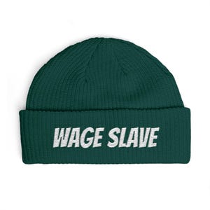 May include: A dark green beanie with the text "WAGE SLAVE" in white block letters. The beanie is made of a ribbed knit material and has a folded brim.