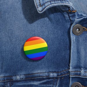 May include: A rainbow pride button pin on a denim jacket.