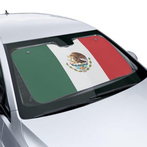May include: A car windshield sunshade featuring the Mexican flag. The sunshade displays the flag's green, white, and red vertical stripes, with the Mexican coat of arms in the white section. The sunshade is installed in a silver car.