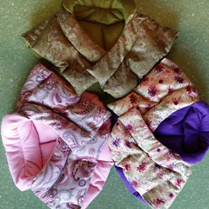 May include: Four handmade neck pillows in different patterns and colors. The pillows are made of fabric with floral and paisley designs. The pillows are filled with a soft material and have a purple, pink, and green color scheme.
