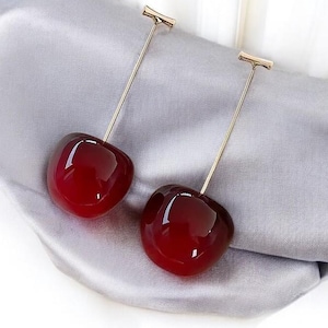May include: A pair of long cherry earrings with gold stems. The cherries are a deep red colour and have a glossy finish.