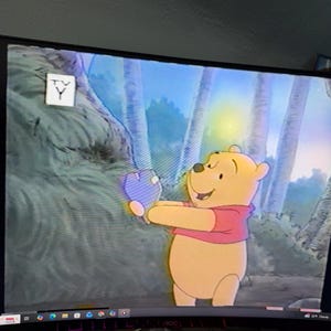 May include: A cartoon still featuring Winnie the Pooh, a yellow bear in a red shirt, holding a blue object. The background depicts a forest scene with tall trees and a blue sky. The TV-Y rating is visible.